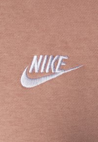 Vitt broderat Nike-logotyp och swoosh på ljusbrunt ribbat tyg.