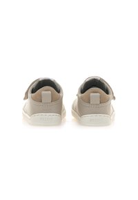 Beige leren sneakers met een klittenbandsluiting en zachte tan accenten. Witte rubberen zolen, ronde vorm en gestikte details.