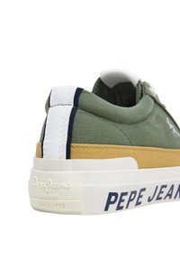 Zelené plátěné tenisky s bílými a námořnickými akcenty, s opálenou mezipodešví a embosovaným logem na patě. Odolná tkanina a jednoduchý design.