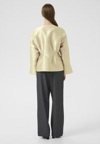 Cream satin long-sleeve top with a fitted bodice, paired with loose grey trousers. Simple neckline, smooth texture, and minimal detailing.