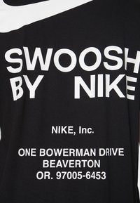 Musta t-paita, jossa on paksu valkoinen teksti: "SWOOSH BY NIKE", "NIKE, Inc." ja osoitetiedot. Pehmeä puuvillakangas ja yksinkertainen malli.