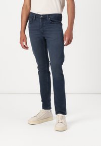 Sötétkék farmernadrág egyenes szabással, denim anyagból. Klasszikus öt zsebes kialakítással és cipzáras, gombos záródással rendelkezik.