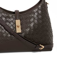 Brown leather handbag, featuring a woven texture, gold hardware closure, and an adjustable strap. Smooth base with side accent.