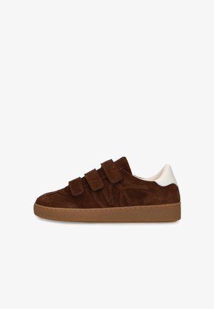 Bruine suède sneaker met drie klittenbandsluitingen, een loopzool van gum en een witte hielaccent, zijaanzicht op een witte achtergrond.