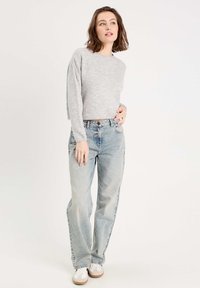 Suéter recortado gris claro, textura suave, ajuste relajado. Jeans de tiro alto azul claro, de pierna ancha. Zapatillas blancas con suelas beige.
