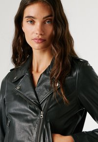 Μαύρο δερμάτινο μπουφάν μηχανής με αιχμηρό γιακά, κλείσιμο με φερμουάρ και μεταλλικές λεπτομέρειες. Υφή με κομψή, εφαρμοστή σιλουέτα.