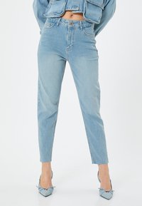 Jeans de mezclilla azul claro con cintura alta, pierna ajustada y dobladillos deshilachados. La tela presenta una textura deslavada con un diseño clásico de cinco bolsillos.