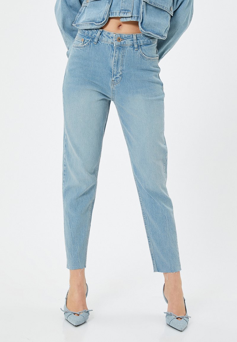 Jeans de mezclilla azul claro con cintura alta, pierna ajustada y dobladillos deshilachados. La tela presenta una textura deslavada con un diseño clásico de cinco bolsillos.