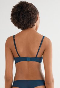 Námořnický modrý bikini top s nastavitelnými ramínky, zapínáním na sponu a hladkým povrchem. Jednoduchý design s minimálním zdobením.