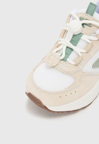Beige Sneaker mit weißen Mesh-Einsätzen und grünen Akzenten. Mit strukturiertem Wildleder, elastischen Schnürsenkeln und Gummisohle. Rundes Zehendesign.