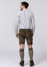 Grau karierter Langarmhemd, braune Lederkurzschlüsse und gemusterte Kniestrümpfe. Erdtöne mit einer strukturierten Verarbeitung.