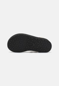 Semelle extérieure en caoutchouc noir avec un motif de grip texturé comportant des formes géométriques ; marqué "Teva" sur le côté.