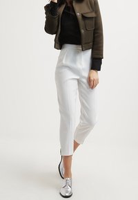 Białe spodnie o prostym kroju, w połączeniu z czarną górą i oliwkowo-zieloną krótką kurtką. Srebrne buty na sznurówki dopełniają stylizację.