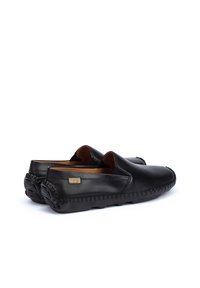 Zapatos negros de cuero tipo mocasín sin cordones, con costuras decorativas. Textura lisa, puntera redonda y diseño minimalista. Presentan un forro de cuero y suela de goma.