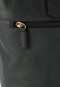 Schwarze, strukturierte Ledertasche mit einem goldenen Reißverschluss und passendem Zubehör. Der Reißverschluss-Anhänger hat einen markanten Akzent mit einem Logodetail.