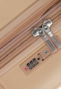 Valigia beige con doppie cerniere argento, un lucchetto a combinazione approvato dalla TSA e superficie testurizzata per una migliore presa. Le linee di design in evidenza migliorano la struttura.