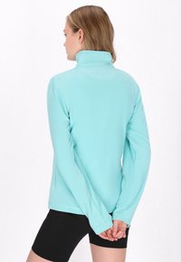 Lys blå fleece-pullover med høj krave, lange ærmer og løs pasform, der har en glat tekstur og ingen synlig hardware.