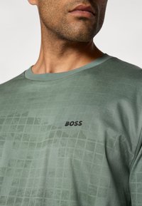 T-shirt en coton vert avec un motif à carreaux subtil, col rond et un logo "BOSS" noir sur le côté gauche de la poitrine.