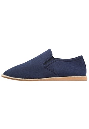Chaussure bleu marine à enfiler avec bout pointu, panneaux latéraux élastiques, dessus en tissu et semelle plate marron clair.