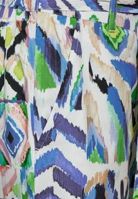 Tessuto multicolore con motivi astratti in tonalità di blu, verde, nero e pesca, con cuciture visibili e una texture liscia.