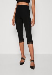 Sorte capri leggings med høj talje og blondekant nederst. Glat tekstur med en tætsiddende pasform. Bæret med sorte spidse hæle.