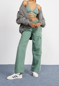 Grünes Zweiteiler-Outfit mit einem verkürzten Bralette mit Logo und hoch taillierten Cargo-Hosen. Kombiniert mit einer grauen Oversize-Jacke und Sneakers.