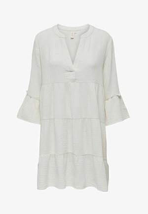 Hvit, teksturert tunika med V-hals, trekvart bell-ermer og et laget design. Har en knappestengning og subtile stingdetaljer.