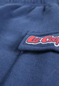 Shorts en tissu bleu marine avec un patch logo blanc et rouge. Texture douce avec taille élastique et coutures détaillées le long des coutures.