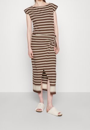 Femme portant une robe midi rayée marron et beige avec un nœud latéral et une fente à l'avant, associée à des sandales blanches douillettes à enfiler.