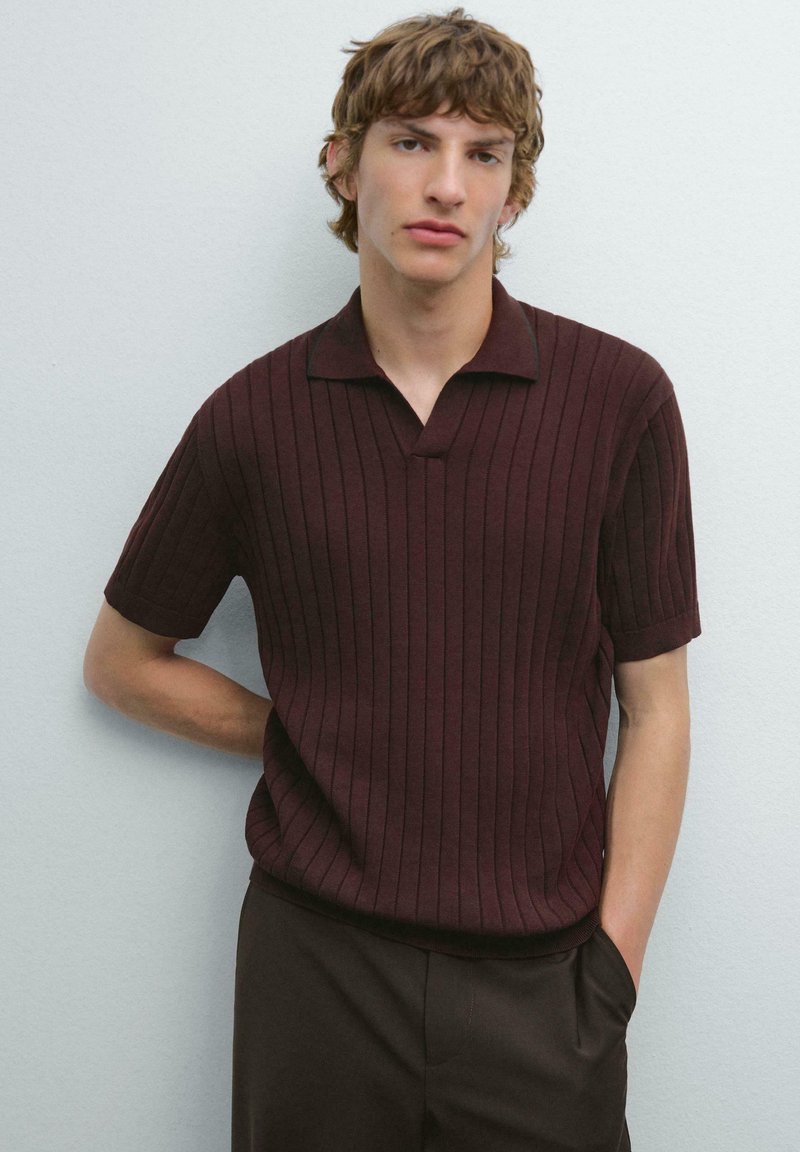 Kortärmad polo t-shirt i burgunderröd med vertikal ribbad textur, krage och avslappnad passform. Kombinerad med mörka byxor.