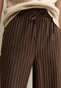Bruine gestreepte broek met een elastische tailleband, voorzien van een strikdetail. Gemaakt van een gladde stof met een subtiele glans.
