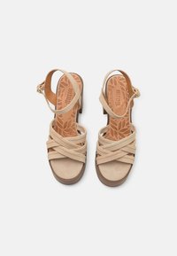 Beige suede sandalen met kruislings geplaatste banden, een gevoerd voetbed en een lage blokhak. Verstelbare enkelband met metalen detail.
