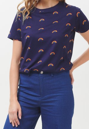 Námořnická modrá trička s krátkým rukávem s potiskem barevných duhov. Měkká tkanina s uvolněným střihem, doplněná o modré džíny s vysokým pasem.