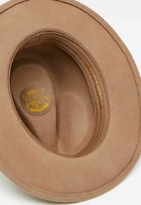 Brown felt hat with a wide brim and soft interior. Features a gold emblem inside and stitched lining detail. Round shape, smooth texture.