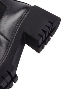 Bottine en cuir noir avec une surface texturée, dotée d'une semelle en caoutchouc noir épaisse avec un motif de semelle prononcé.