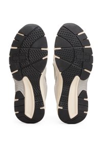 Semelle de chaussure avec une surface texturée en caoutchouc noir, présentant une semelle intermédiaire beige lisse et un motif de bande de roulement triangulaire distinctif pour une meilleure adhérence.