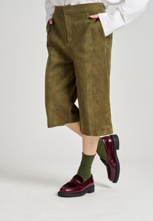 Pantalones culottes de ante verde oliva con frente plano, bolsillos laterales y detalles cosidos. Combinados con mocasines burdeos y calcetines verdes.