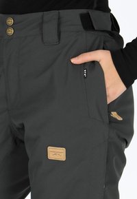 Mörkgrå utomhusbyxor i slitstark tyg; har två guldknappar, ett kardborreband och en läderbadge med "Swedemount"-logotyp.