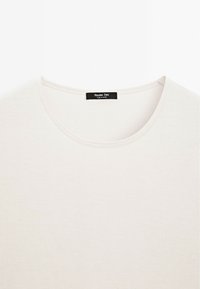 Light beige crew-neck t-shirt with a smooth, soft texture and subtle ribbing; features a black label at the neck with brand information.