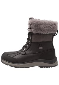 Bota negra impermeable de UGG con parte superior de cuero texturizado, cuello de pelo sintético gris, diseño con cordones y suela de goma resistente.