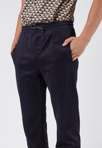 Granatowe spodnie z elastycznym paskiem w talii, bocznymi kieszeniami i zwężanym krojem, uszyte z gładkiego materiału o delikatnej fakturze.