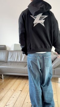 Sweatshirt preta com capuz e um grande gráfico de estrela prateada nas costas; combinada com jeans azul claro com bolsos traseiros.