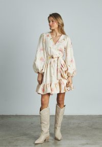 Blumenkleid aus leichtem Stoff mit Ballonärmeln und gerafftem Saum, in sanften Rosa- und Gelbtönen, kombiniert mit hellen Cowboy-Stiefeln.