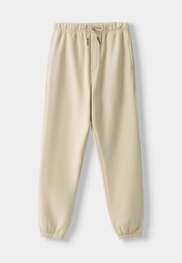 Beige joggerbyxor med elastisk midja, dragsko, sidofickor och elastiska manschetter på en vit bakgrund.