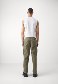 Pantaloni cargo verde oliva con molte tasche laterali, abbinati a una maglietta senza maniche bianca. Tessuto liscio, vestibilità regolare e materiale resistente.