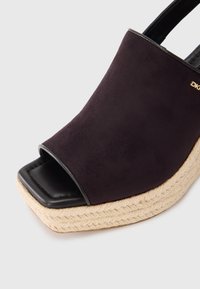 Μαύρο ανοιχτό πέδιλο πλατφόρμας από σουέντ με τυλιγμένη πλατφόρμα από τζούτα, διαθέτει  μαλακό μαύρο δερμάτινο πέλμα και διακοσμητικό χρυσό λογότυπο.