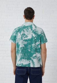 Camisa de manga corta en color azul turquesa con un patrón abstracto en blanco, hecha de una tela ligera, con cuello y un corte relajado.