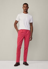 T-shirt bianca a maniche corte abbinata a chinos rosa brillante. I pantaloni presentano una vestibilità su misura e pieghe frontali, abbinati a scarpe marroni.