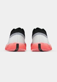 Ténis desportivos com parte superior em cinza e preto, sola rosada e detalhes texturizados. Apresenta um calcanhar reforçado e um padrão de tração em borracha.