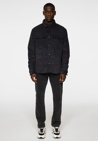 Svart kordjacka i manchestertyg med två bröstfickor, ihopparad med svarta jeans och vita sneakers. Tyget har ett strukturerat vertikalt ribbat mönster.